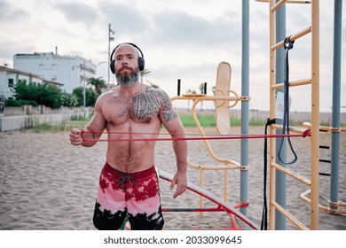 Athlete Man Doing Calisthenics Workout With A Resistance Rubber Band At The Beach.