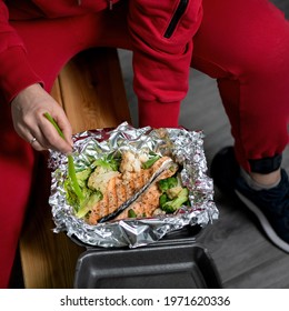 Athlete Man eating omega-rich seafood, red fish with vegetables wrapped in foil. Takeaway food concept. Square format or 1x1 for posting on social media.