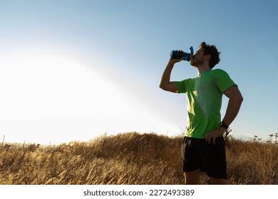 Athlete man hydrates after running in nature at sunset. Copy space