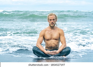 Athlete man meditating in ocean waves on a beach