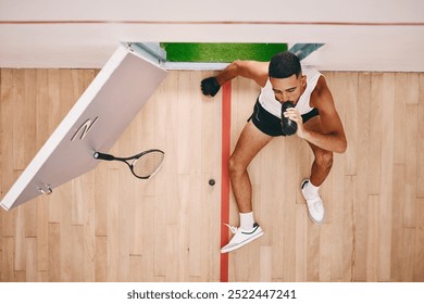 Athlete, man and relax with drinking water on court from squash competition, fitness break and sports burnout. Above, male person and racket for challenge, tired and game hydrate of match performance - Powered by Shutterstock