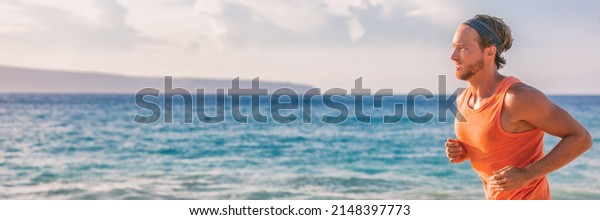 Athlete man runner sweating tired during\
endurance workout on beach running at sunset portrait panoramic\
banner. Active\
lifestyle