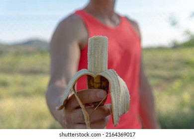 Athlete man showing a banana that is bitten. Frontal image of a young athlete who is holding an open banana that he has previously nibbled with the intention of maintaining a healthy diet.