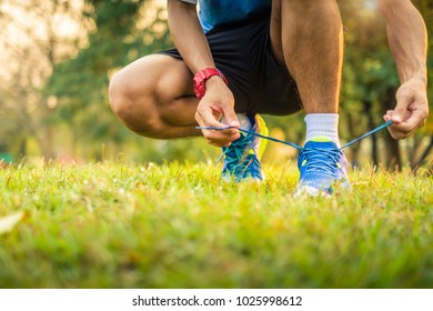 athlete man tying running shoes lace in the park outdoor, sportman ready for jogging on the road outside, asian Fitness walking and exercise on green grass in morning. wellness and sport concepts