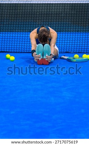 Athlete performing forward hamstring flexion stretches on a blue padel court in front of a net.
