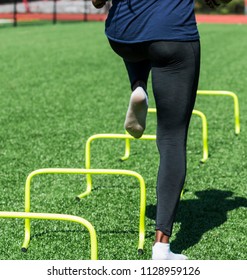 An Athlete Is Performing Speed And Agility Drills Wearing White Socks, Balck Spandex And Blue Shirt On A Green Turf Field During Track Practice.