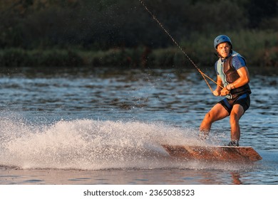 An athlete performs a trick on the water. Park at sunset. Wakeboard rider. - Powered by Shutterstock