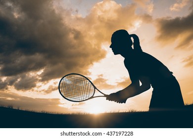 Athlete playing tennis with a racket against landscape with sunset