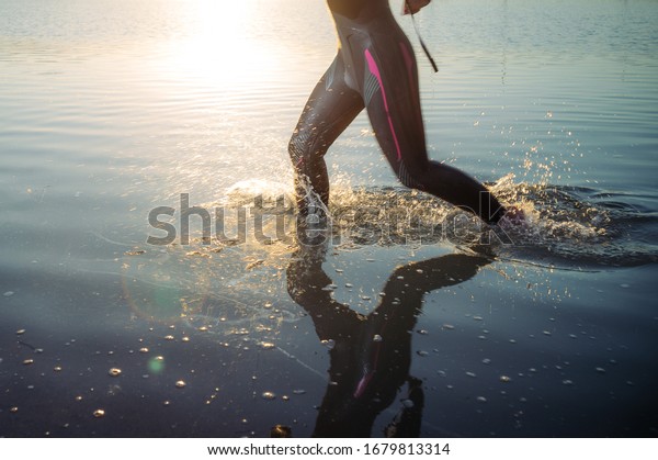 Athlete posing\
with wetsuit by lake at sunset.\
