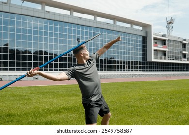 Athlete preparing to throw javelin on field near stadium. Javelin thrower standing with javelin in ready position with focus and determination under clear sky - Powered by Shutterstock