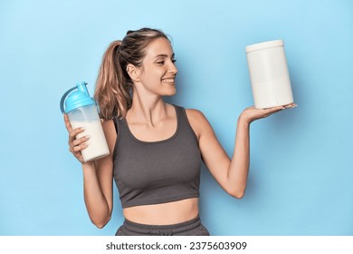 Athlete with protein shake and container in blue studio - Powered by Shutterstock