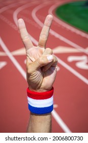 Athlete With Red, White And Blue Wrist Sweatband Making A V-sign For Victory With Hand At A Running Track