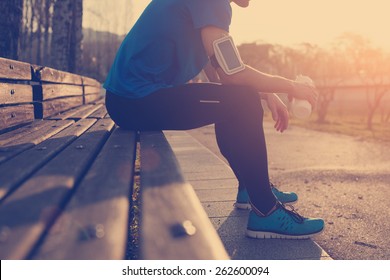 Athlete resting on bench in park at sunset after running with bottle of water (intentional sun glare and vintage color) - Powered by Shutterstock