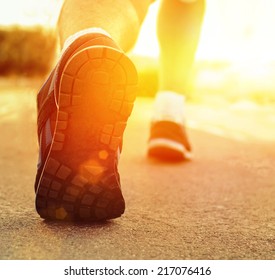 Athlete Runner Feet Running On Treadmill Closeup On Shoe.Mans Fitness With The Sun Effect Of Fall Autumn Colors In The Background 