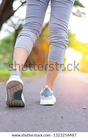 Athlete runner feet woman running in green park along road at sunrise morning.