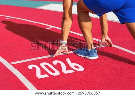 Athlete runner in a pose ready to start on a red treadmill line with the inscription numbers 2026. The concept of the beginning of the New Year.
