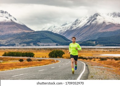 Athlete Runner Running Road Race In Amazing Mountain Range Landscape In New Zealand. Man Run Exercise Long Distance Cardio Training Outdoors In Cold Fall Weather.