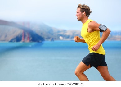 Athlete running man - male runner in San Francisco listening to music on smartphone. Sporty fit young man jogging by San Francisco Bay and Golden Gate Bridge. Jogger training with smart phone armband, - Powered by Shutterstock