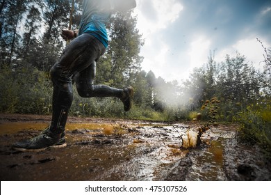 Athlete running through the dirty puddle in the rural road