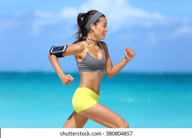 Athlete Running Woman Runner Listening To Music On Her Phone Sports Armband With Touchscreen And Headphones Earphones On Summer Beach. Fitness Girl Jogging Fast Training Cardio And Glutes.