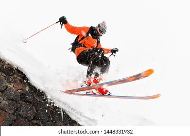 The Athlete Skier On A Light Background With A Jump Moves Off The Roof Of A Snow-covered Hut With Flying Flakes Of Snow. The Concept Of Winter Ski Sports