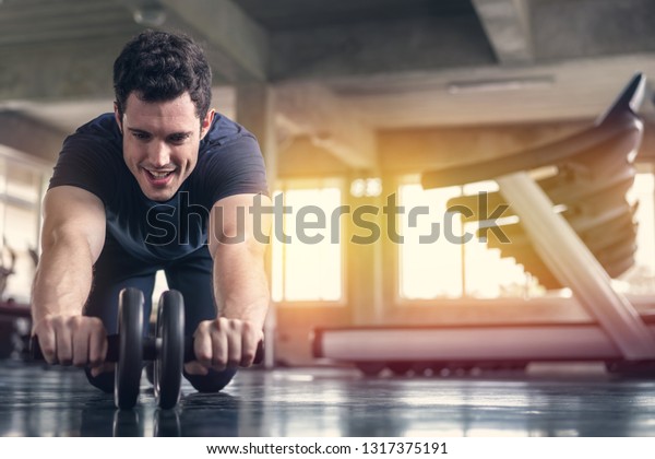 Athlete sporty man doing\
exercise with abs roller wheel to strengthen his abdominal muscle\
in gym.