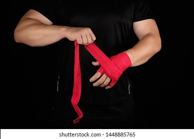 athlete stand in black clothes and wrap his hands in red textile elastic bandage before training, black background - Powered by Shutterstock