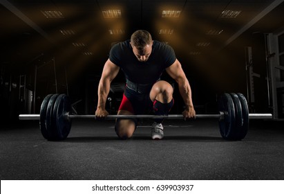 Athlete is standing on his knee and near the bar in the gym and is preparing to make a deadlift