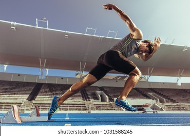 Athlete starting his sprint on an all-weather running track. Runner using starting block to start his run on running track in a stadium.
