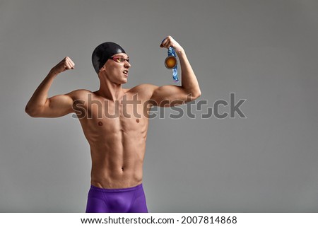 Athlete swimmer with a medal in his hands celebrating a victory, gray background, copy space