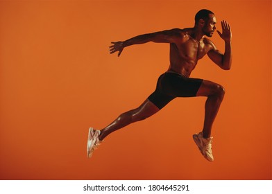 Athlete taking long stride forward during sprint. Bare chested athlete running hard on orange background. - Shutterstock ID 1804645291