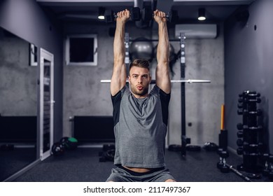 The athlete trains dumbbells in the gym on a dark grey background. Sport concept and taking care of the figure. The man lifts dumbbells, cares for his muscles. Weightlifting, sports training