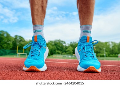 Athlete wearing bright blue running shoes on red stadium track during training. Sportsman legs in sport sneakers at racetrack. Fitness and healthy lifestyle concept - Powered by Shutterstock