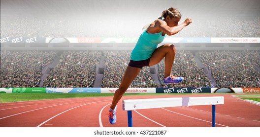 Athlete woman jumping a hurdle against view of a stadium