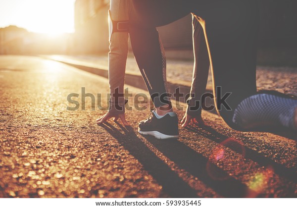 Athlete woman in running start pose on the\
city street. Sport tight clothes. Bright sunset, blurry background.\
Horizontal