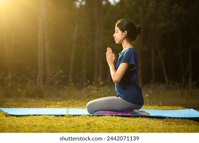 athlete women kneeling and sitting in a vajrasana yoga position and doing prayer pose yoga in the park at a sunset time , side angle view - Powered by Shutterstock