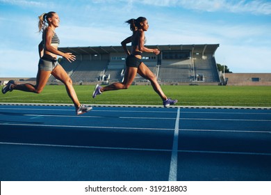 Athletes Arrives At Finish Line On Racetrack During Training Session. Young Females Competing In A Track Event. Running Race Practicing In Athletics Stadium.