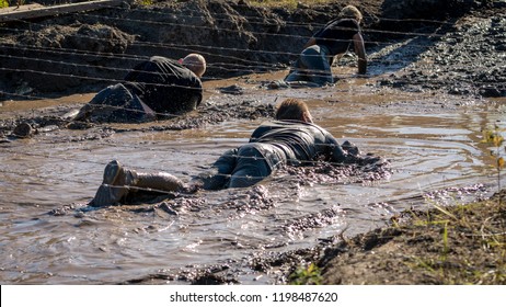 Athletes crawling under barbed wire in mud, obstacle course race 