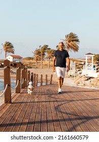 Athletic 60-years Old Man Walking Together With His Dog Jack Russell Terrier By The Sea.