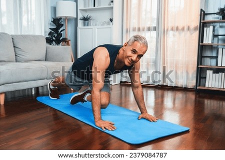 Athletic and active senior man doing exercise on fit mat with plank climbing at home exercise as concept of healthy fit body lifestyle after retirement. Clout