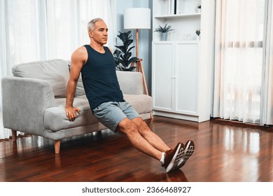 Athletic and active senior man using furniture for effective targeting muscle with push up at home exercise as concept of healthy fit body lifestyle after retirement. Clout