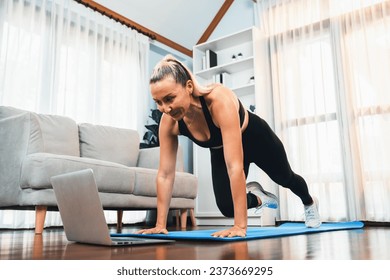 Athletic and active senior woman doing exercise on fit mat with plank climbing at home exercise while watching online exercising video as concept of healthy fit body lifestyle after retirement. Clout