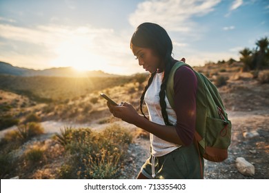 athletic african american woman with backpack looking at smart phone while hiking in red rock canyon nevada