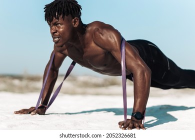 Athletic African man , doing push-ups with elastic band as additional difficulty, outdoors, Athlete doing dynamic workouts by pulling rubber elastic bands