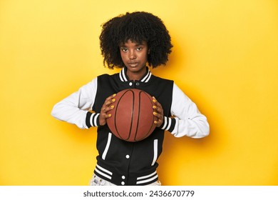 Athletic African-American teenage girl holding a basketball on a yellow studio backdrop. - Powered by Shutterstock