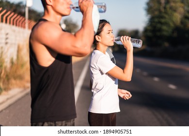 Athletic Asian couple wearing face mask drinking water on road after exercising together during coronavirus or covid-19 outbreak. Putting off protective masks. Work out in quarantine. - Powered by Shutterstock