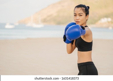 Athletic Asian girl on the beach in summer in a sports black suit leading a boxing training. direct hand strike and look at the camera. Sport lifestyle.