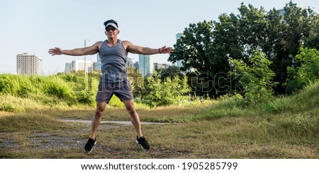 An athletic asian guy does jumping jacks at a open field near the city. Cardiovascular fitness. Working out outdoors.