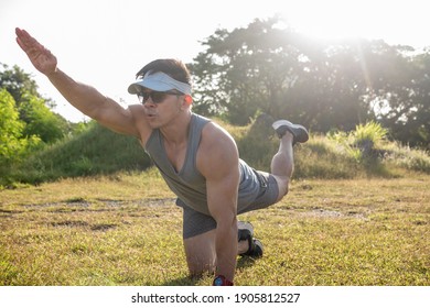 An Athletic Asian Man Performs Bird Dogs On The Grass Of An Open Field. Lower Back And Ab Workout.