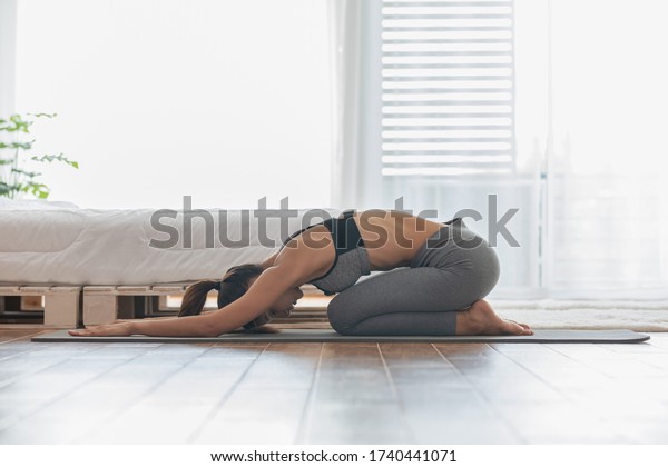 Athletic Asian\
woman practice yoga Child\'s pose to meditation in bedroom after\
wake up in the morning Feeling so comfortable and relax,Healthcare\
and yoga at home\
Concept